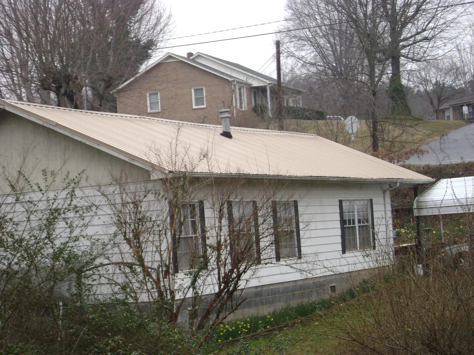 Tan metal roof on a white sided house set into a hillside — Commercial Roofing by Roofing Brothers in Grandview